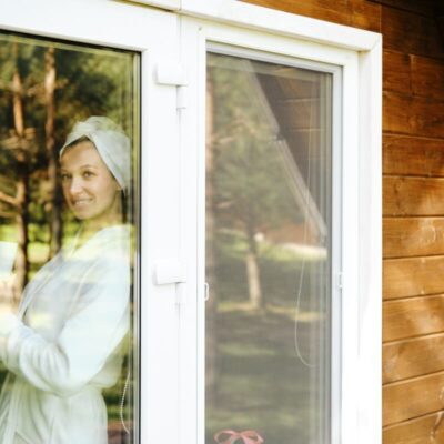 Kobieta stoi przy oknie z moskitierą okienną, trzymając filiżankę.